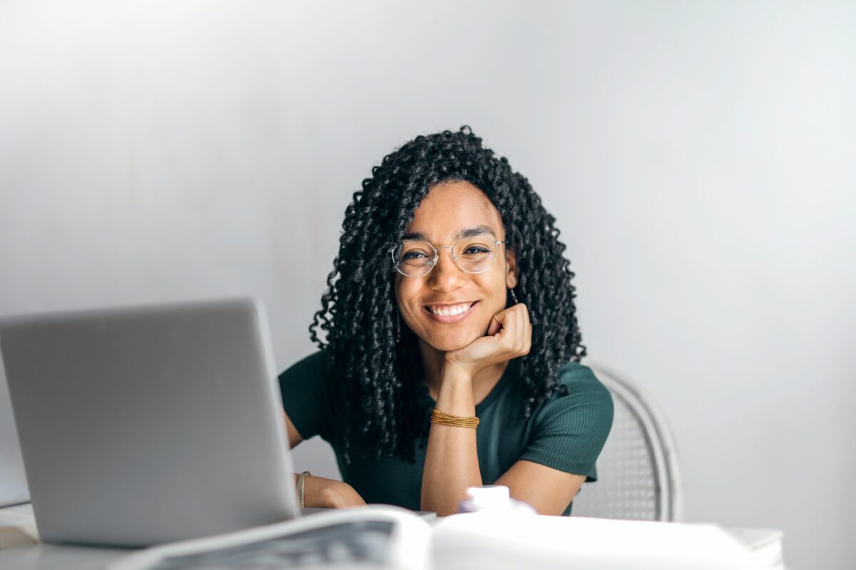 Beautiful woman smiling in front of a gray laptop, wearing eyeglasses and a bracelet. She is looking directly at the camera.