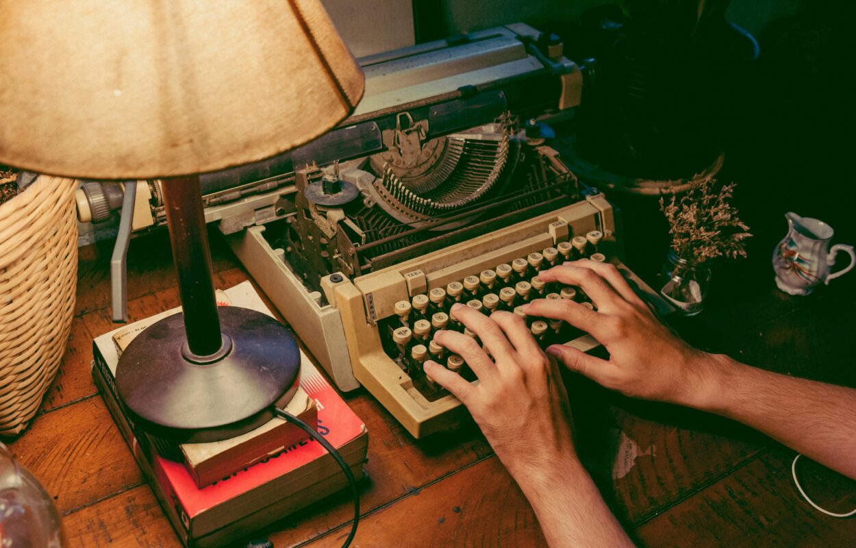 Person typing on an old fashioned typewriter under the light of a lamp