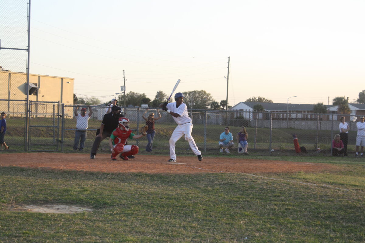 Baseball player in white uniform getting ready to swing the bat. A catcher and umpire prepare behind him.