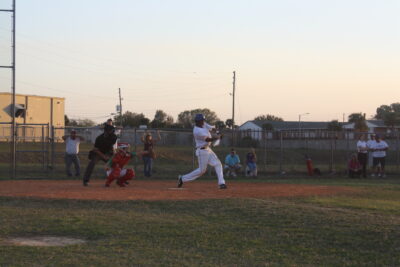 Baseball batter taking a swing at a pitch. The catcher has his glove out ready to catch the ball and the umpire watches attentively.