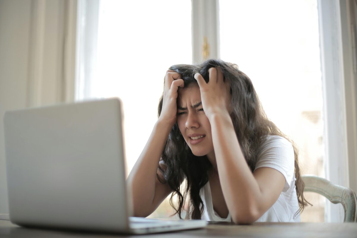 Woman behind a laptop with her hands on her head, showing signs of frustration.